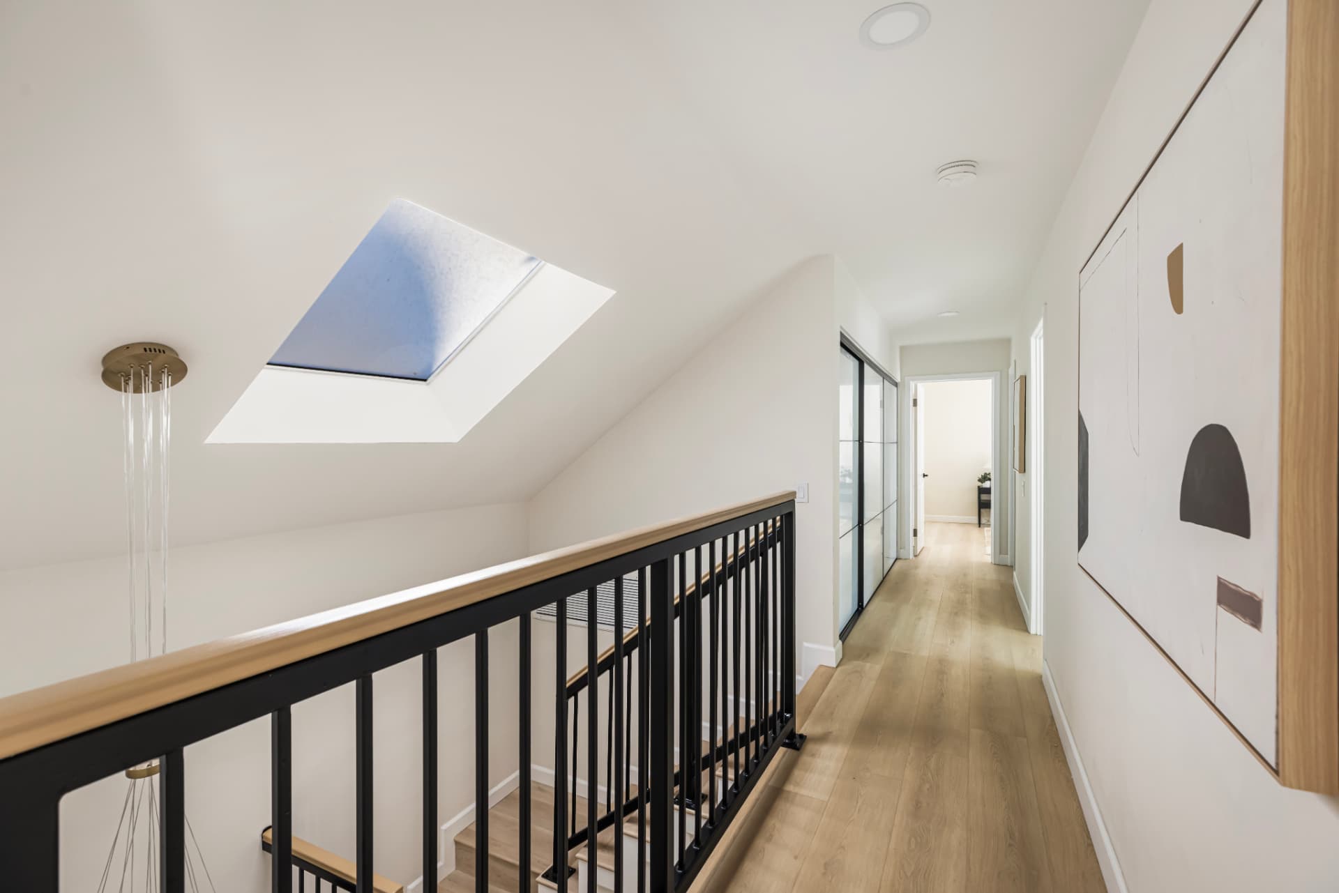 Skylit upstairs hallway with wood floors and black railing